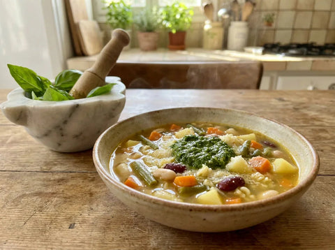 Soupe au pistou provençale en bol rustique : haricots, courgettes et pâtes dans un bouillon doré, cuillerée de pistou de basilic au centre