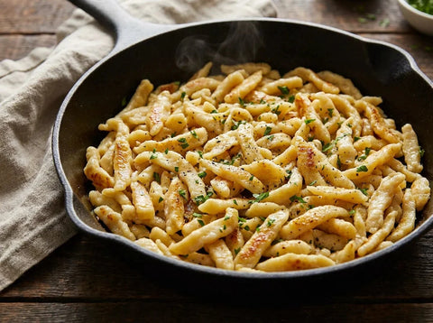 Spaetzles alsaciens dorés au beurre noisette dans une poêle en fonte, parsemés de persil ciselé