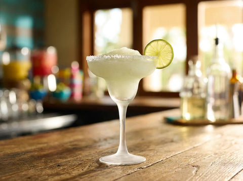 Frozen Margarita granitée vert pâle dans un verre à margarita à bord givré de sel avec rondelle de citron vert