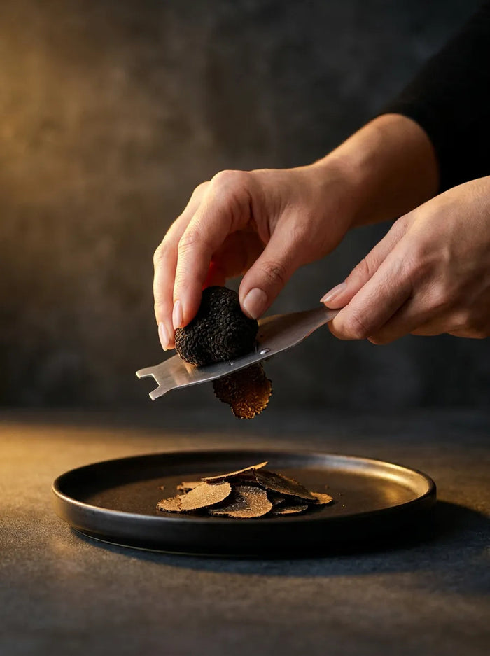 Mains tranchant une truffe noire du Périgord à la mandoline