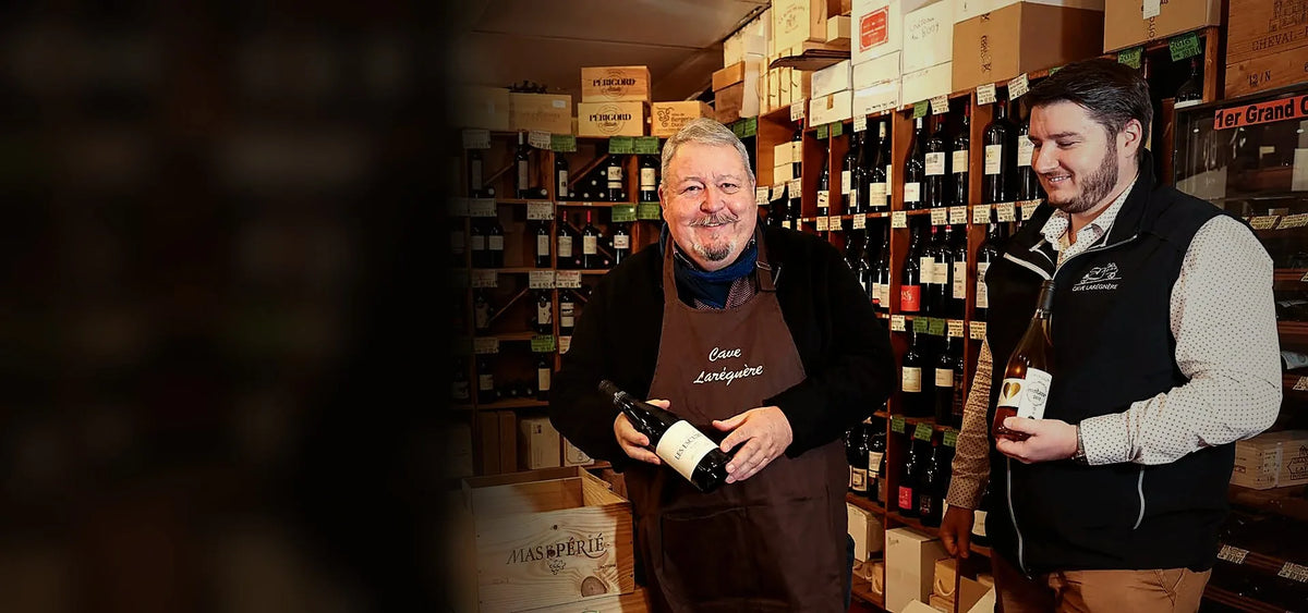 Michel et Grégoire Baraton dans la cave, entourés de bouteilles et de caisses de vin